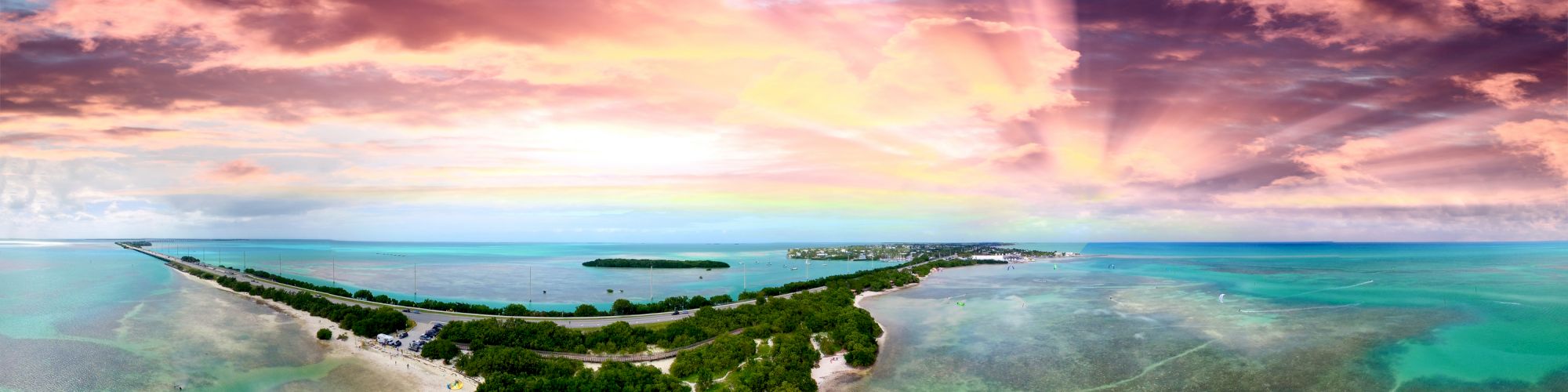 A stunning aerial view of a tropical island with lush greenery, surrounded by turquoise waters and a vibrant sunset painting the sky in shades of pink and orange.