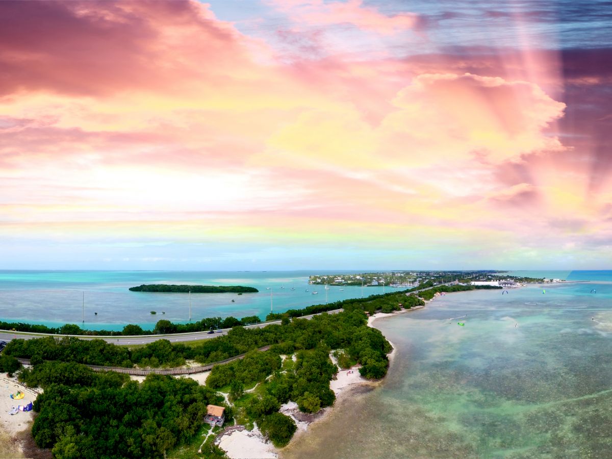 A panoramic view of a tropical island with clear turquoise waters, lush greenery, and a vibrant sunrise or sunset in the sky ends the sentence.