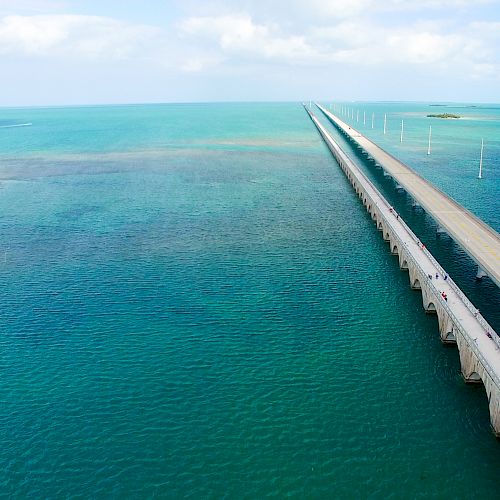A long bridge stretches over clear blue water, connecting islands under a bright, partly cloudy sky, showcasing an impressive feat of engineering.