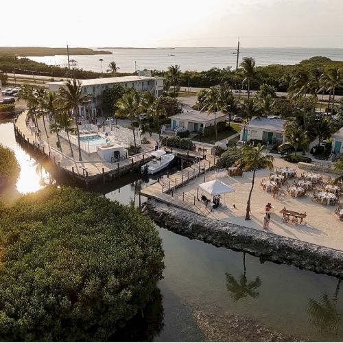 Aerial view of a coastal resort with a pool, waterfront, and surrounding greenery; tables and chairs set up outdoors, probably for an event.