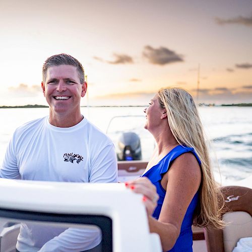 A man and a woman are smiling and enjoying a boat ride on the water during sunset, with a cloudy horizon in the background.