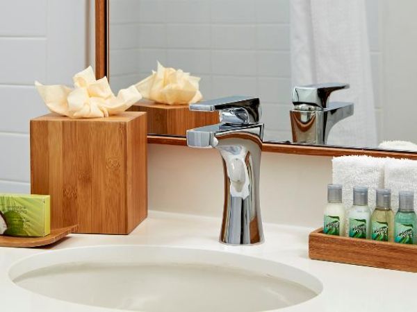 A clean bathroom sink area with tissue box, soap, faucet, mirror, and a tray with small lotion bottles and rolled white towels.
