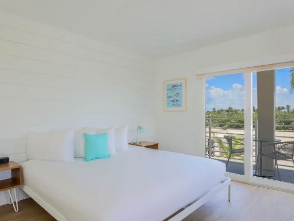 A modern, bright bedroom with a large bed, nightstands, wall art, and sliding doors opening to a balcony with a scenic view.