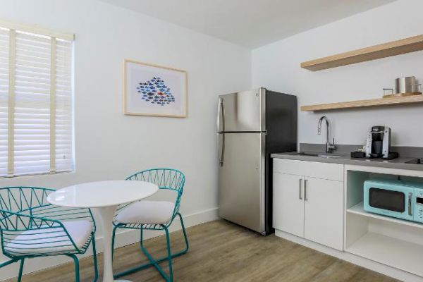 A compact kitchen with a table and two chairs, a refrigerator, microwave, coffee maker, and shelves with kitchen items.