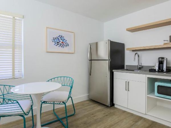 A small, modern kitchen with a table and chairs, refrigerator, open shelves, sink, coffee maker, and microwave on shelving under the counter ends the sentence.