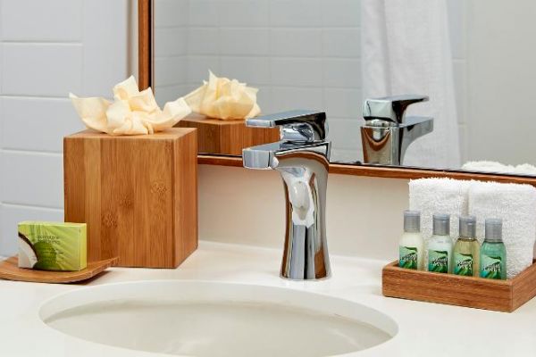 A neatly organized bathroom countertop features a modern faucet, tissue box, soap, and a tray with towels and small toiletries, all in wooden holders.