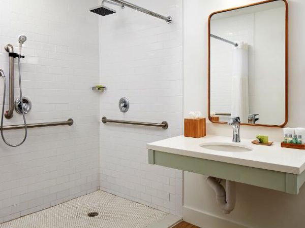 A modern bathroom with a walk-in shower, white tiles, a wall-mounted sink, mirror, towel rack, and toiletries displayed on the sink.