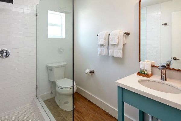 The image shows a modern bathroom with a shower, toilet, sink, large mirror, and wall-mounted towels in a bright and clean setting.