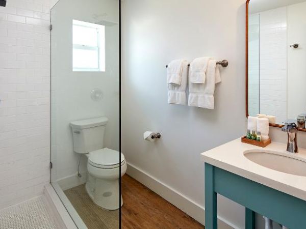 The image shows a modern bathroom with a shower, toilet, sink, large mirror, and wall-mounted towels in a bright and clean setting.