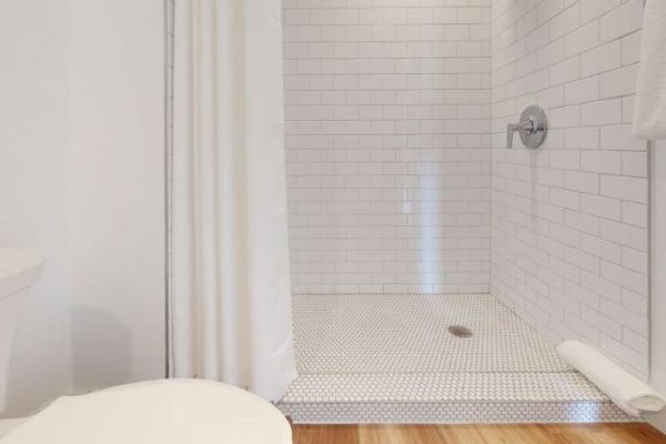 The image shows a bathroom with a white tiled shower, a shower curtain, and a toilet. There is also a towel hanging nearby.