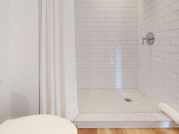 The image shows a bathroom with a white tiled shower, a shower curtain, and a toilet. There is also a towel hanging nearby.