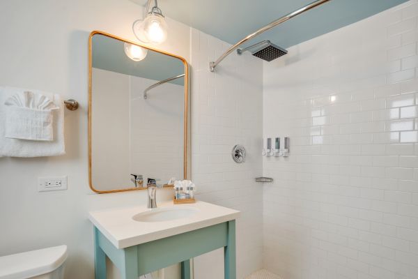 A modern bathroom features a vanity with a mirror, a towel rack, and an open walk-in shower with white subway tiles and a rain showerhead.