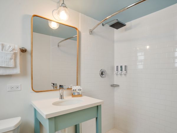 A modern bathroom features a vanity with a mirror, a towel rack, and an open walk-in shower with white subway tiles and a rain showerhead.