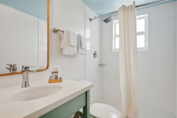 A modern bathroom with a sink, a mirror, a towel rack with towels, a shower with a curtain, and a window, all decorated in white.