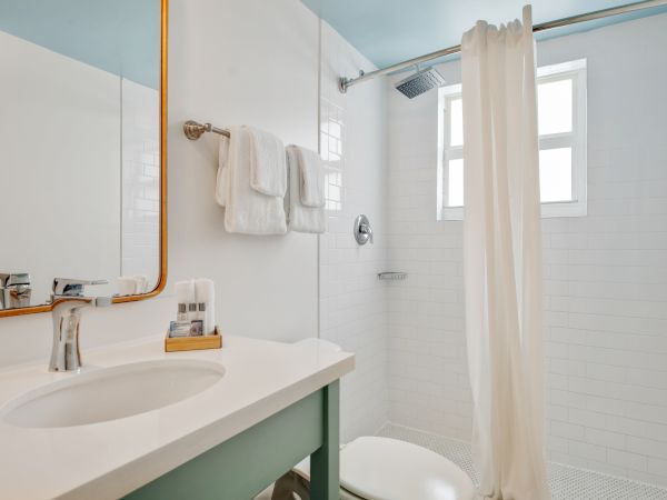 A modern bathroom with a sink, a mirror, a towel rack with towels, a shower with a curtain, and a window, all decorated in white.
