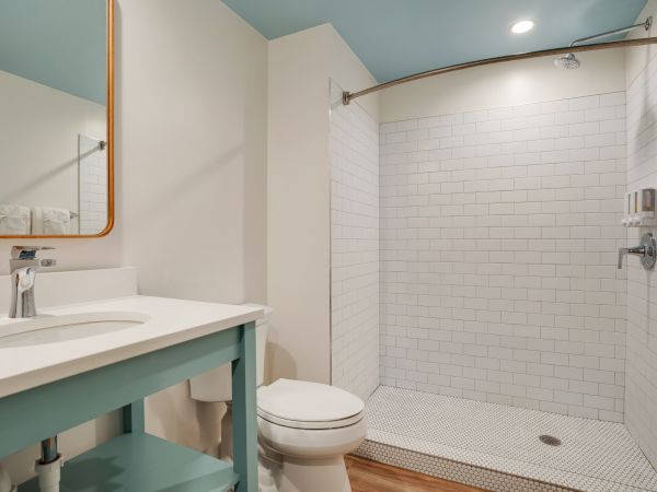 The image shows a modern bathroom with a minimalist design, featuring a vanity, toilet, and walk-in shower with white tiles and a glass partition.
