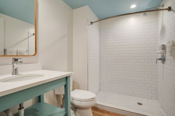 The image shows a modern bathroom with a minimalist design, featuring a vanity, toilet, and walk-in shower with white tiles and a glass partition.