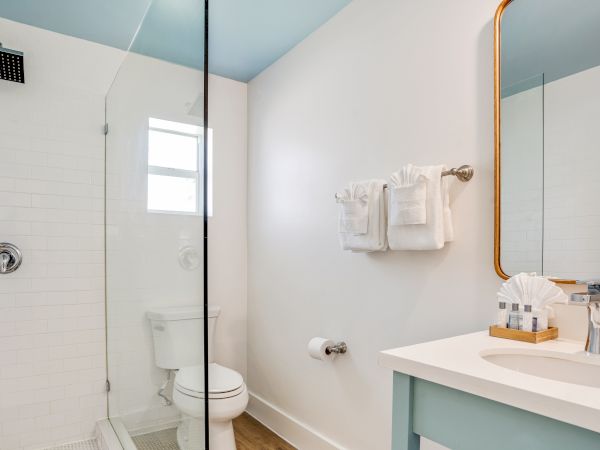 A modern bathroom with a glass-enclosed shower, toilet, sink with vanity, mirror, and white towels on a rack.