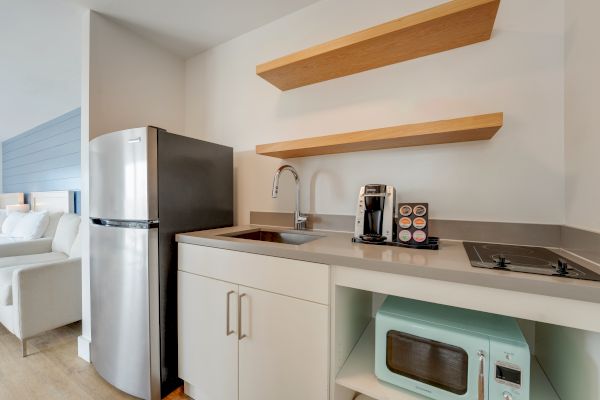 A compact kitchenette with a refrigerator, sink, coffee maker, microwave, stove, and open shelves is visible in the image.