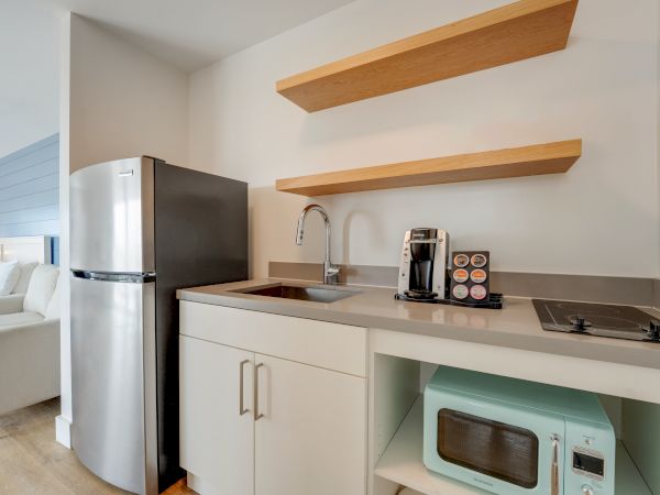 A compact kitchenette with a refrigerator, sink, coffee maker, microwave, stove, and open shelves is visible in the image.