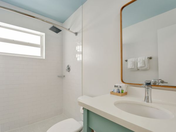 This image shows a clean bathroom with a shower area, a sink with a faucet, a large mirror, toiletries on the counter, and a window.