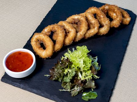 The image features a plate with fried onion rings, a small dish of dipping sauce, and a side of mixed greens for garnish.