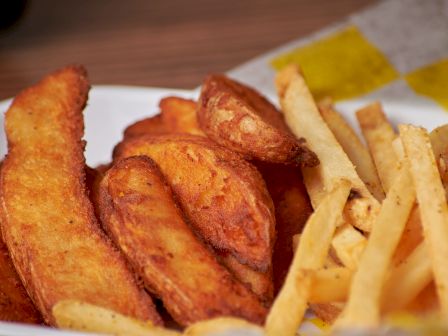 The image shows a plate with both potato wedges and French fries placed together, ready to be served and eaten.