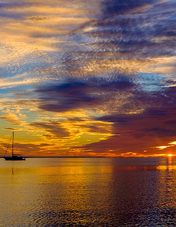 A tranquil scene with a sailboat silhouetted against a vibrant sunset sky, featuring colorful clouds reflecting on calm water.