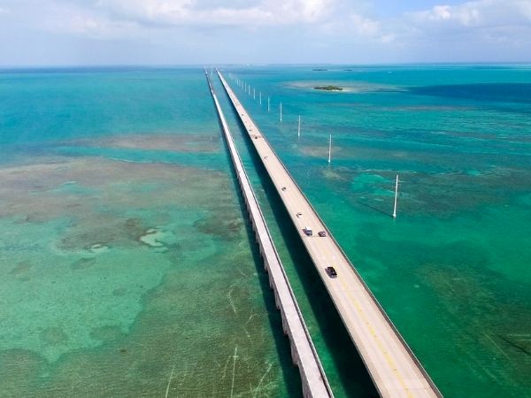 A long bridge extends over turquoise sea, connecting islands with shallow, clear waters below and a bright, sunny sky above.