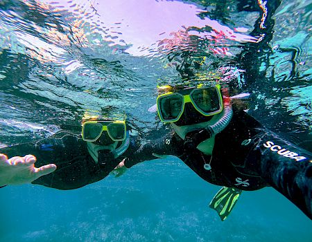 Two snorkelers swim underwater with bright green masks and gear, sending bubbles and splashing water in a vivid ocean scene!