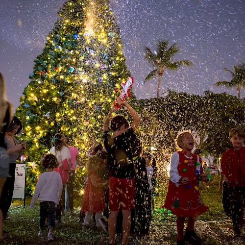 A brightly lit Christmas tree farm parade as children in holiday outfits dance through falling confetti under golden lights.