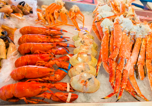 A seafood market tray packed with raw orange prawns and long lobster-like shellfish on ice.