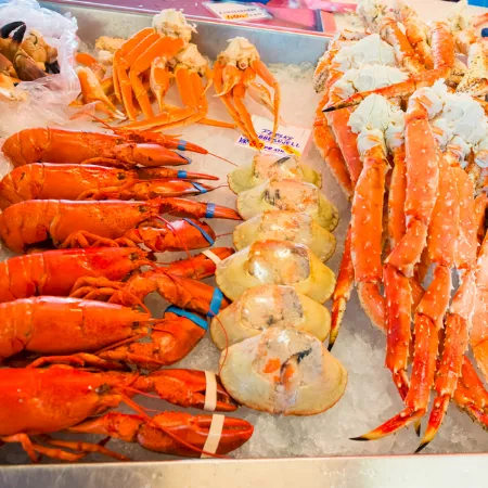 A seafood market tray packed with raw orange prawns and long lobster-like shellfish on ice.