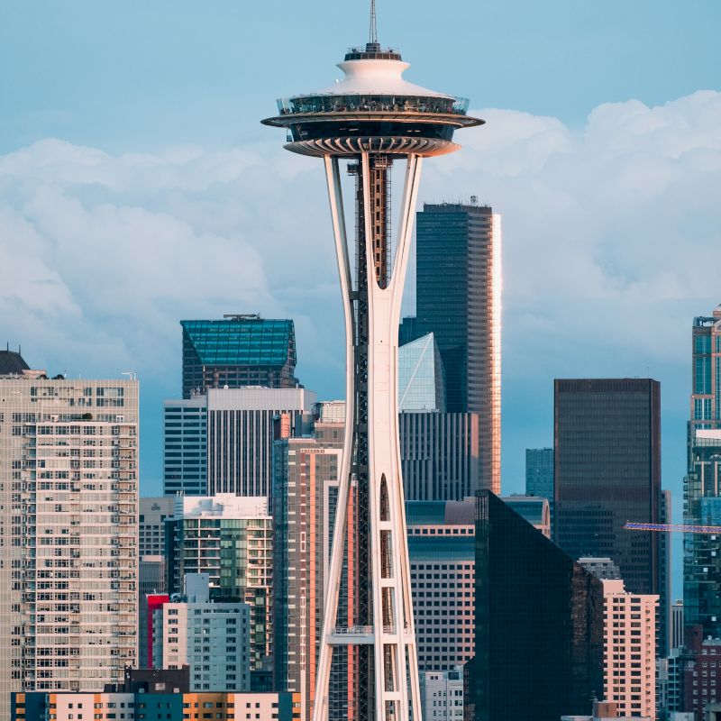 The image features the Seattle Space Needle with surrounding modern buildings and a partly cloudy sky in the background.