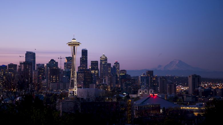 This image shows the Seattle skyline at dusk, featuring the Space Needle and Mount Rainier in the background, with downtown buildings illuminated.