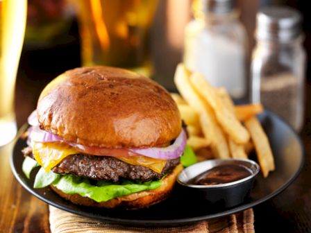 A cheeseburger with lettuce, onions, and a side of fries and dipping sauce on a plate, accompanied by salt, pepper shakers, and a drink in the background.